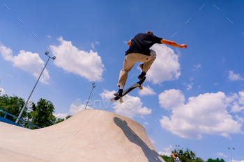 A young guy skater does a stunt on the edge of a skatepool against a backdrop of sky and clouds