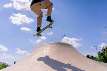 A young guy skater does a stunt on the edge of a skatepool against a backdrop of sky and clouds