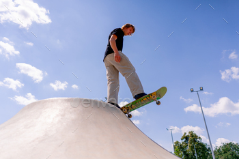 A young guy skater does a stunt on the edge of a skatepool against a backdrop of sky and clouds
