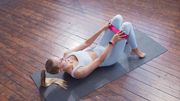 Young and sporty girl in sportswear is using resistance band while doing at home.