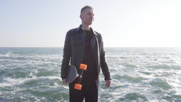 Young Man Holds His Longboard Standing By the Sea