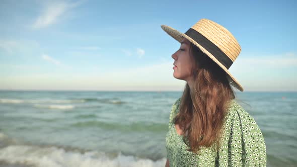Romantic Portrait of Attractive Caucasian Young Woman in Green Dress and Straw Hat on the Seashore