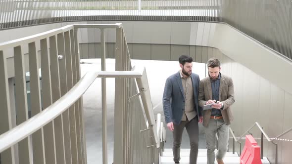 Two young bearded men walking upstairs business district using digital tablet