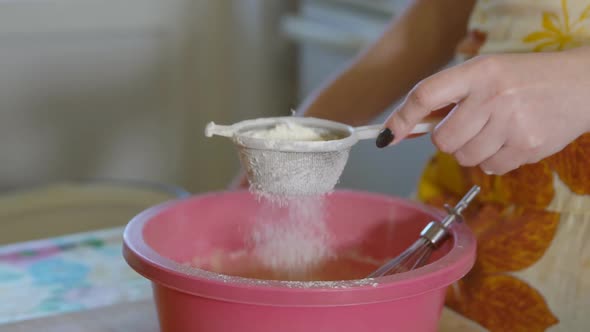 Woman Sifts the Flour Through a Sieve in the Kitchen