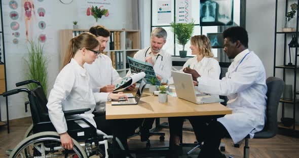 Male and Female Doctors, One Colleague in Wheelchair Get Aquainted with Different Reports