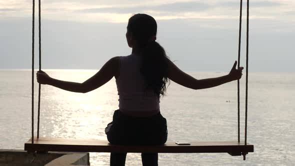 Rearview of Young Asian Woman Sitting and Relaxing on the Swing at the Beach