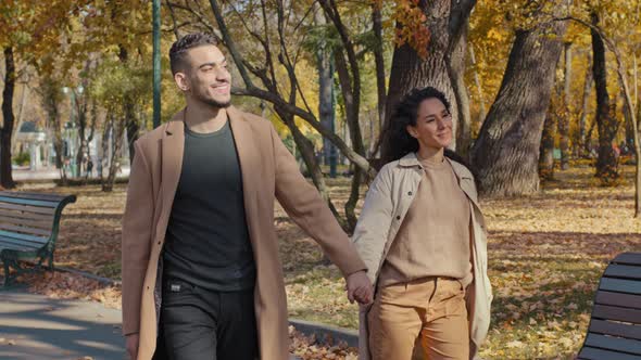 Young Hispanic Couple Walking in Autumn Park Guy and Girl Holding Hands Lovers Have Fun Chatting