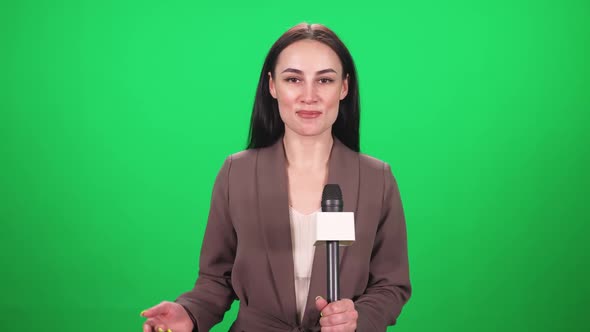 Female Reporter in Suit Looks Into the Camera and Speaks Into a Microphone on a Green Background