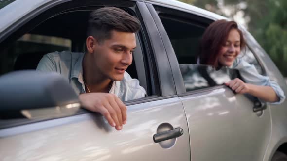 Happy Loving Young Man Talking with Joyful Woman Sitting in Car in Forest