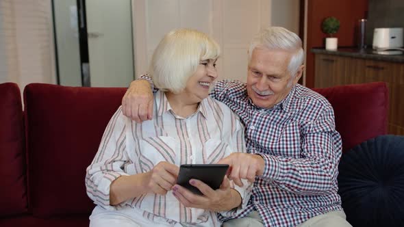 Senior Pensioner Couple with Digital Tablet Pc Computer at Home. Resting on Sofa in Cozy Living Room