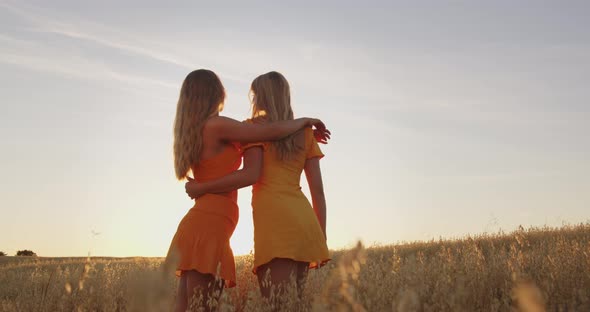 Two Blondes are Standing in a Field at Sunset