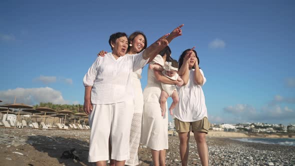 Cheerful Asian Women and Baby Girl Pointing Away Talking Standing on Sunny Picturesque Mediterranean