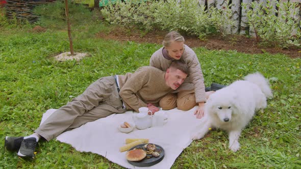 A Young Couple a Man and a Woman on a Picnic in the Garden with Their White Dog in Slowmotion