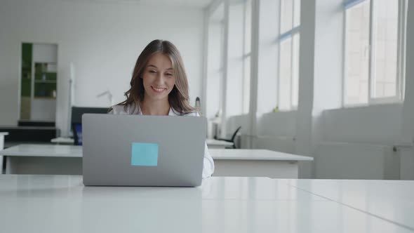 Happy Girl Sits on Her Grey Laptop in White Shirt