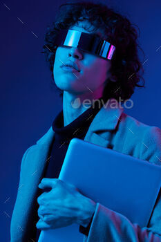 Portrait of a stylish male hacker with a laptop and futuristic glasses in blue light, Blue Perennial