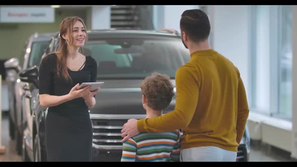 Back View of Adult Caucasian Man Choosing Automobile with Son in Car Dealership