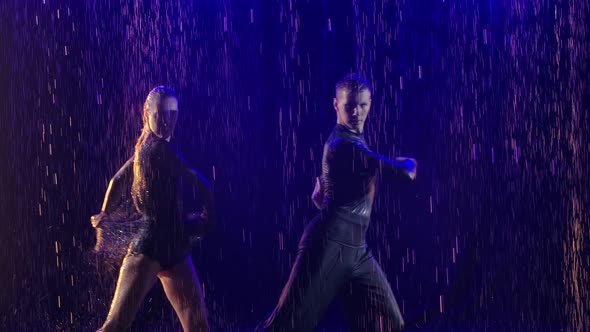 Couple Dancing Jive in the Rain on a Blue Backlight Background. Young Dancers Move Along the Surface