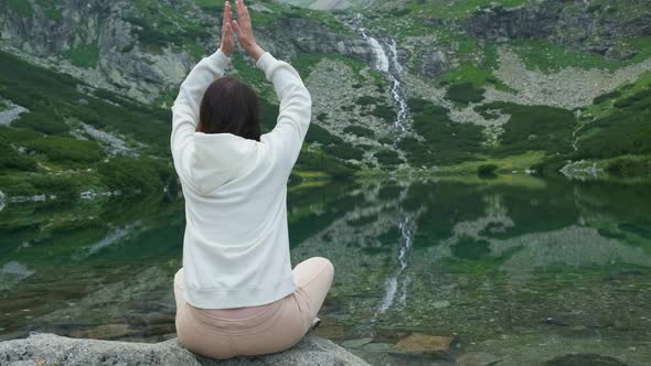 Young Woman Meditating and Holding Up Hands Under the Head with Amazing View on the Lake