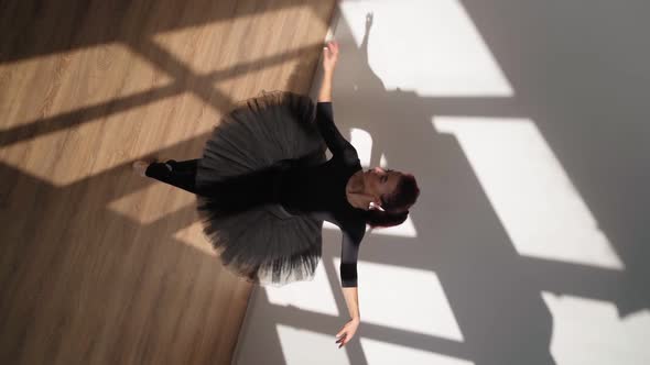 Ballerina in Black Tutu Gracefully Dances Against White Wall in Bright Sunlight