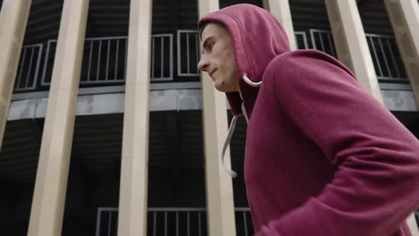 Jogger in Hood Running Against Modern Building in Slow Motion