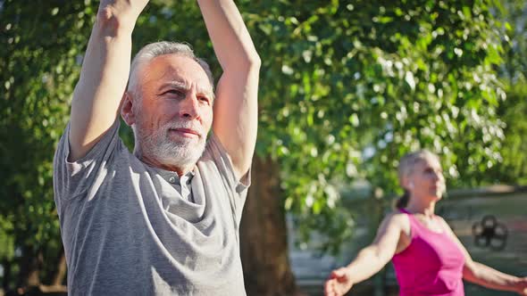 Elderly Man and Woman Raise Hands Up Practicing Yoga