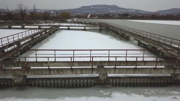 Frozen lake in winter, aerial drone shot from above, concrete walkways in lake, dark, cloudy and moo