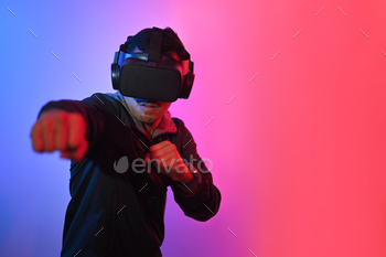 Young man having fun playing boxing game in VR glasses throwing punches in the air