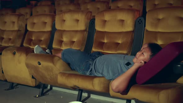 A Boy Laying Down on Armchair in Cinema