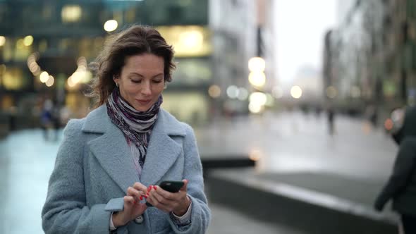 Charming Woman is Walking on Street and Viewing Social Nets in Smartphone Communicating Online