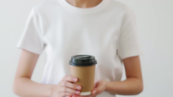 Hand holding a brown paper coffee cup and black cap on white background