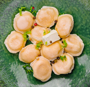 pelmeni with butter and greens on green plate