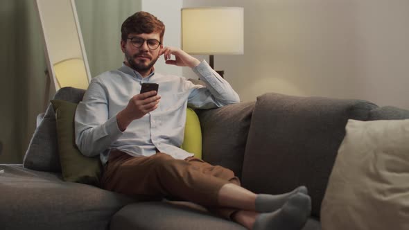 A European Man Lies on the Sofa and Looks at the Phone