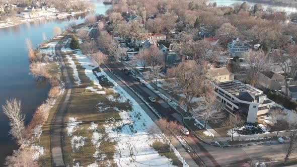 aerial footage following a car on a nice neighborhood, road by the lake shores during a sunny aftern