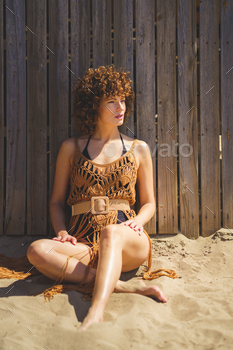 Sensual woman in crochet beach cover up sitting on sand