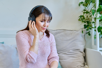Middle-aged woman in headphones listening to audio, music, audiobook, communication