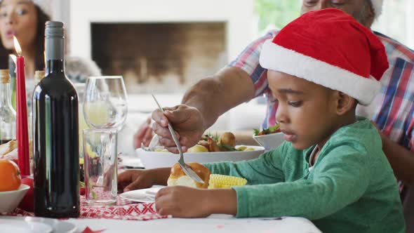 Happy african american multi generation family wearing santa hats and celebrating meal