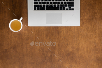 Laptop and cup of tea on a wooden desktop, top view.