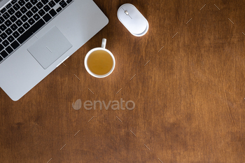 Laptop and cup of tea on a wooden desktop, top view.