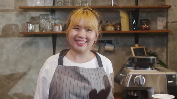 Portrait young Asian woman barista feeling happy smiling at urban cafe.