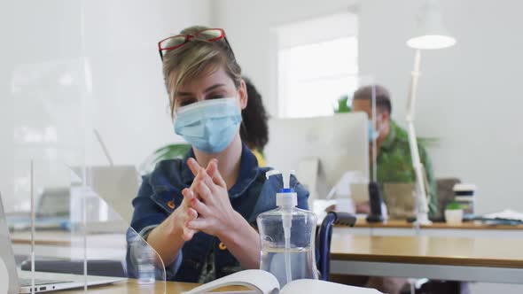 Woman wearing face mask sanitizing her hands at office