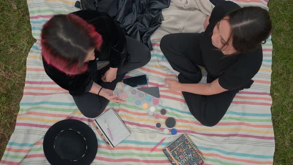 Birds Eye Over Two Girls on Black Clothes Sitting on a Colored Mat Chatting About Cosmetics Makeup