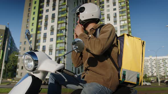 The Male Courier Puts on a Helmet Starts a Scooter and Leaves to Deliver Orders