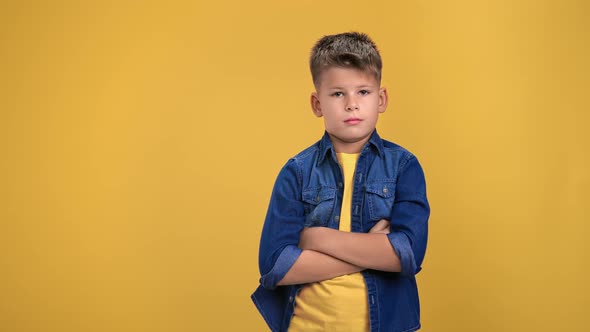 Pensive Confident Male Kid Posing with Crossed Hands Upset Face Expression Isolated on Orange