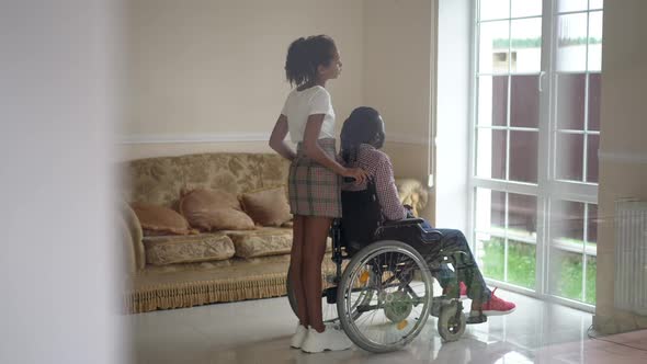 Side View Teenage Daughter Talking in Slow Motion with Disabled Father in Wheelchair Looking Out the