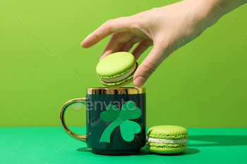 Green cup with clover, macaroons and hand on green background
