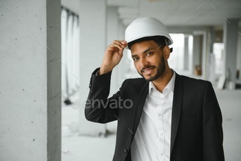 Indian construction site manager standing wearing helmet, thinking at construction site.
