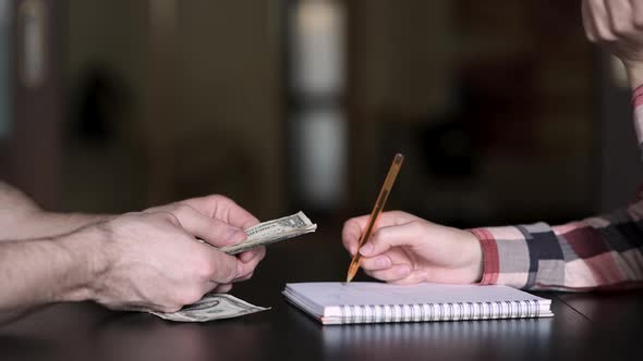 Counting money at home. Male hands count dollars, and a woman makes notes