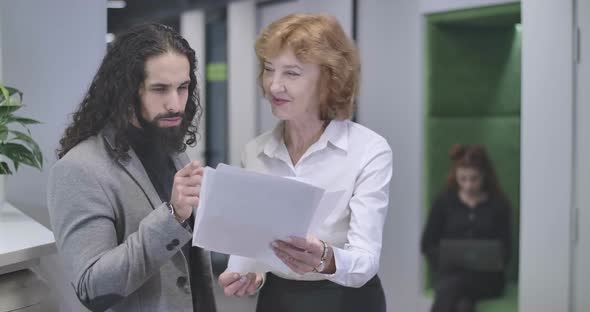 Portrait of Positive Middle Aged Caucasian Woman and Young Middle Eastern Man Standing with Paper