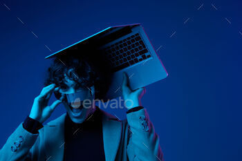 Portrait of stylish man hacker with laptop and futuristic glasses in blue light, cyber security