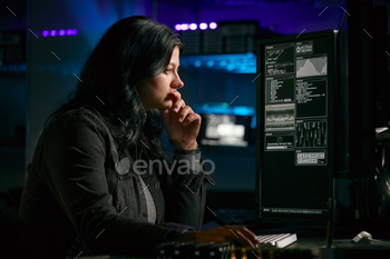 Low Key Lighting Shot Of Female Computer Hacker Sitting In Front Of Screens Breaching Cyber Security